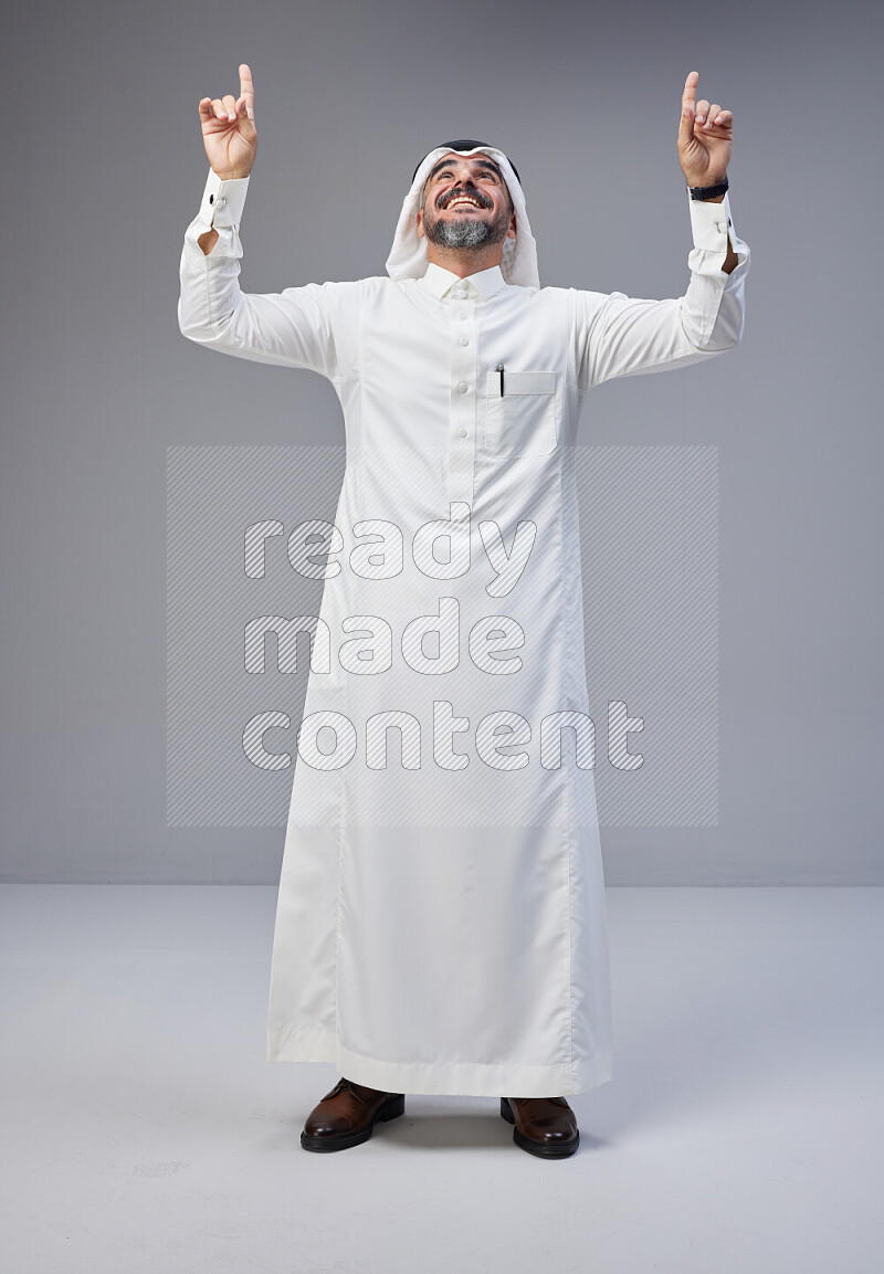 Saudi man Wearing Thob and white Shomag standing interacting with the camera on Gray background