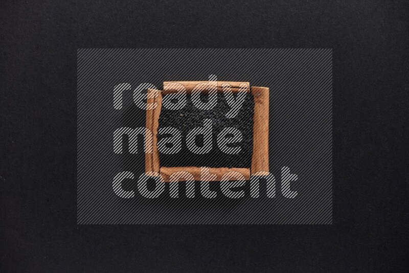 أربعة من أعواد القرفة مكونة شكل مربع بداخلها حبة البركة علي خلفية سوداء