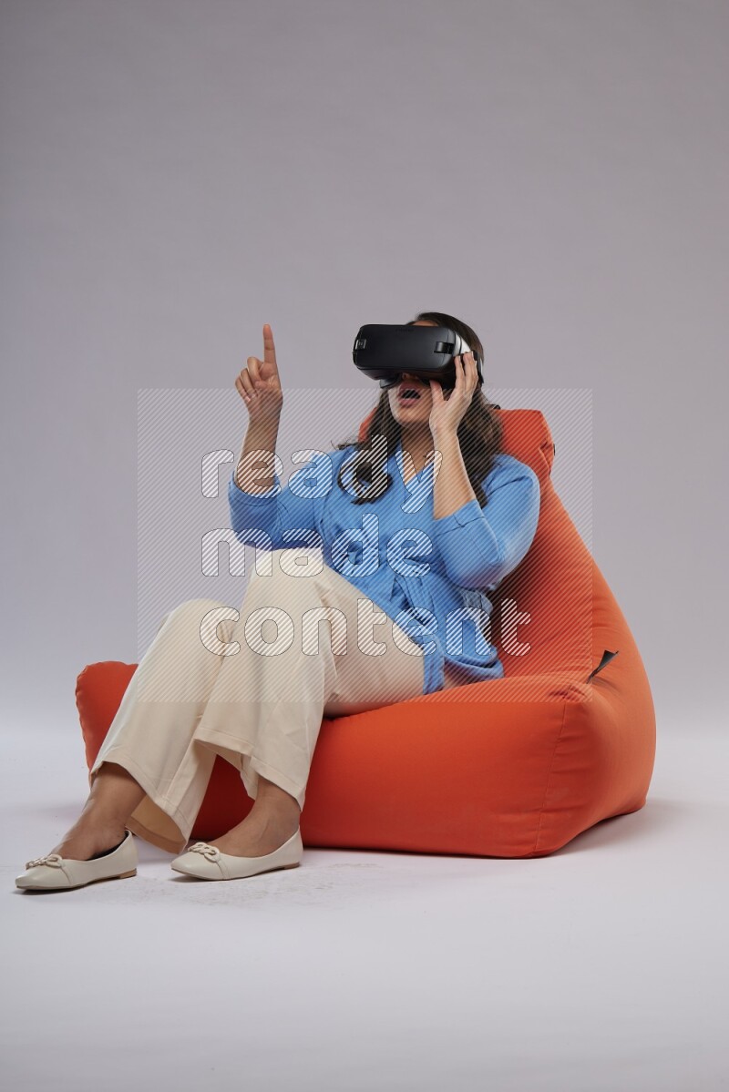 A woman sitting on an orange beanbag and gaming with VR