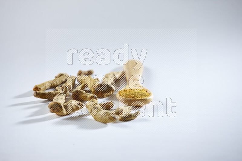 ملعقة خشبية ممتلئة ببودرة الكركم مع أصابع الكركم المجففة بجانبها على خلفية بيضاء