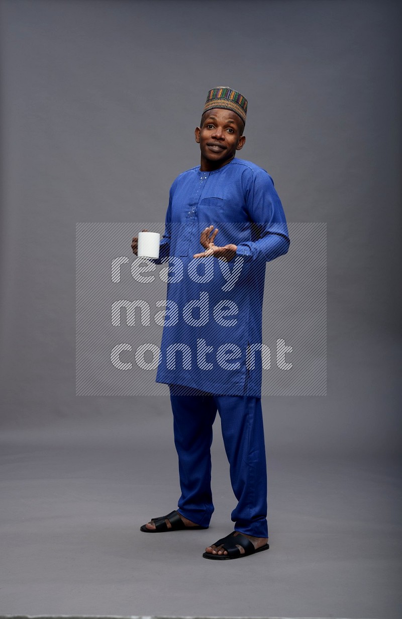 Man wearing Nigerian outfit standing holding mug on gray background