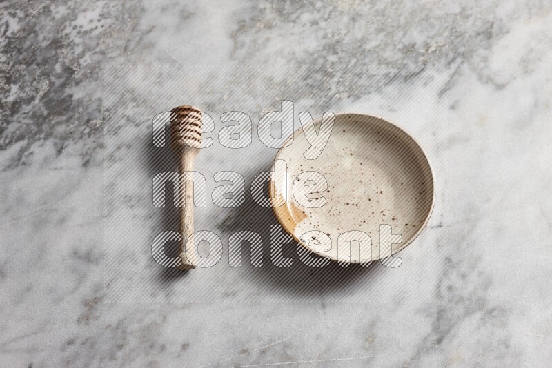 Multicolored pottery plate with wooden honey dipper on the side on grey marble background