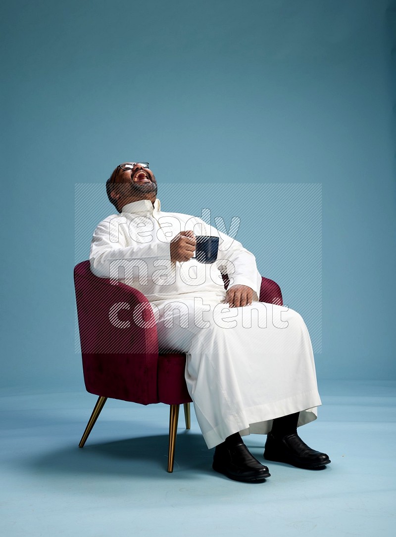 Saudi Man without shimag sitting on chair drinking coffee on blue background
