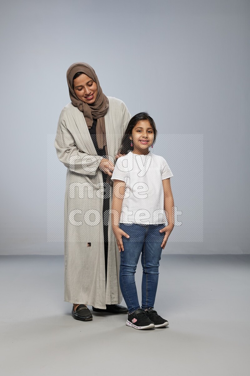 Mom standing styling hair for her daughter on gray background