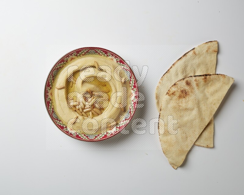 Hummus in a red plate with patterns garnished with pine nuts on a white background