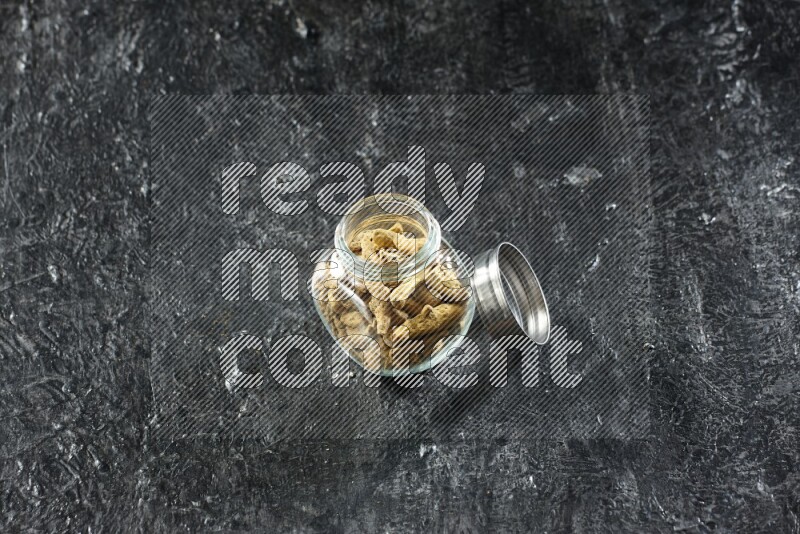 وعاء زجاجي للتوابل ممتلئ بأصابع الكركم المجففة على خلفية سوداء