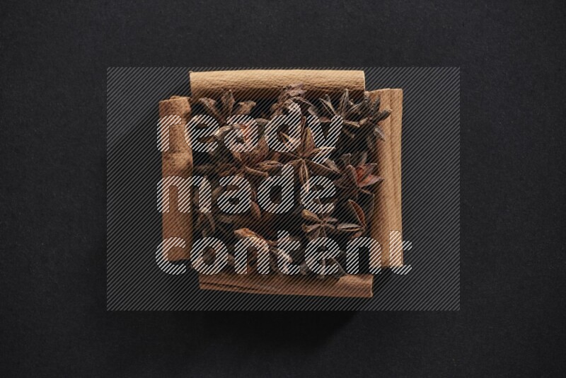 A single square of cinnamon sticks full of star anise on black flooring