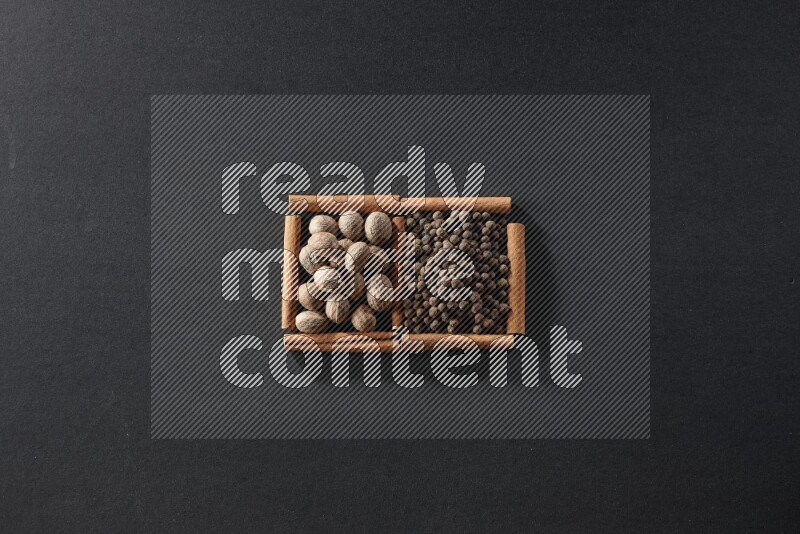 مربعان من أعواد القرفة ممتلئان بجوزة الطيب وحبوب الفلفل الحلو علي خلفية سوداء