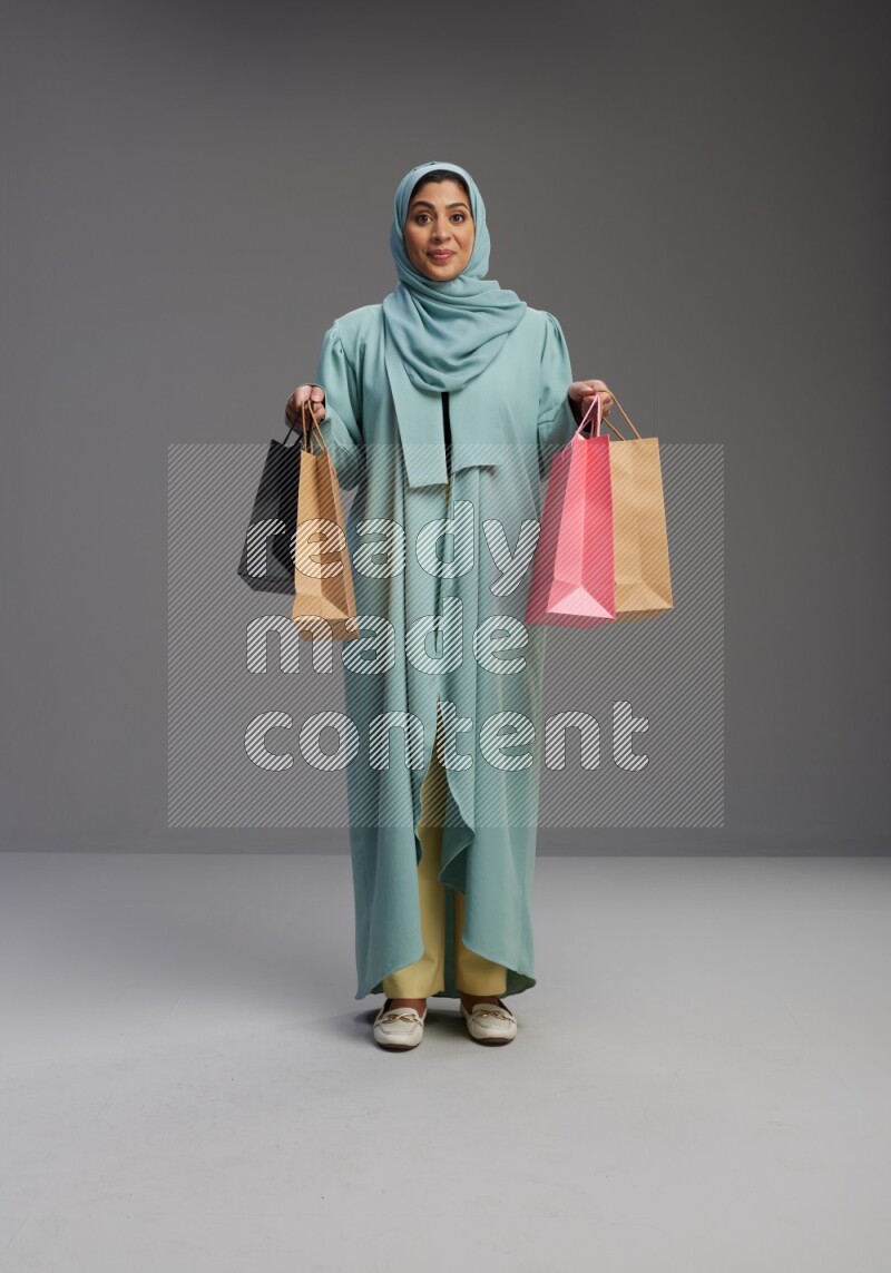 Saudi Woman wearing Abaya standing holding shopping bag on Gray background
