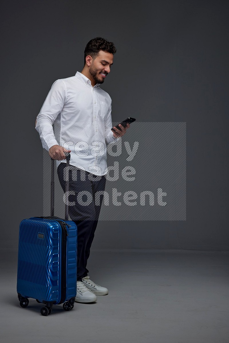 A man wearing smart casual holding luggage eye level on a gray background