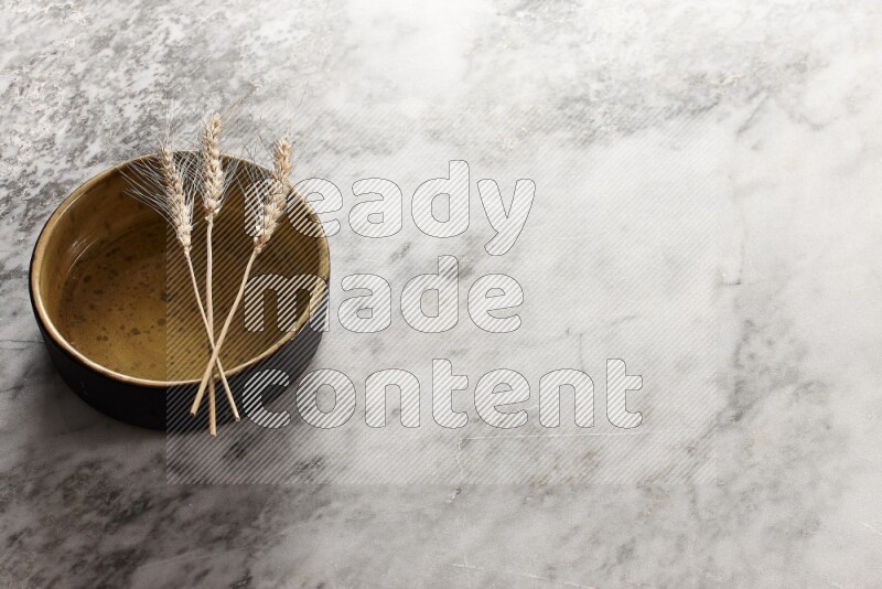 Wheat stalks on multicolored pottery oven plate on grey marble background