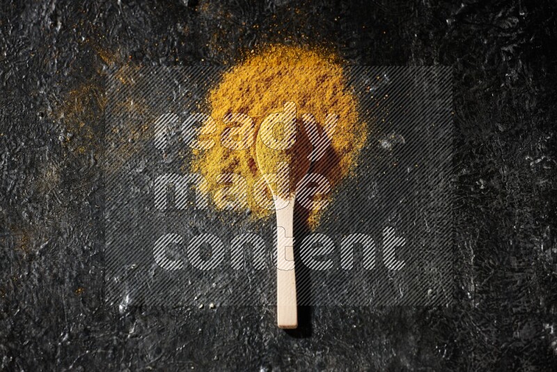 A wooden spoon full of turmeric powder on textured black background