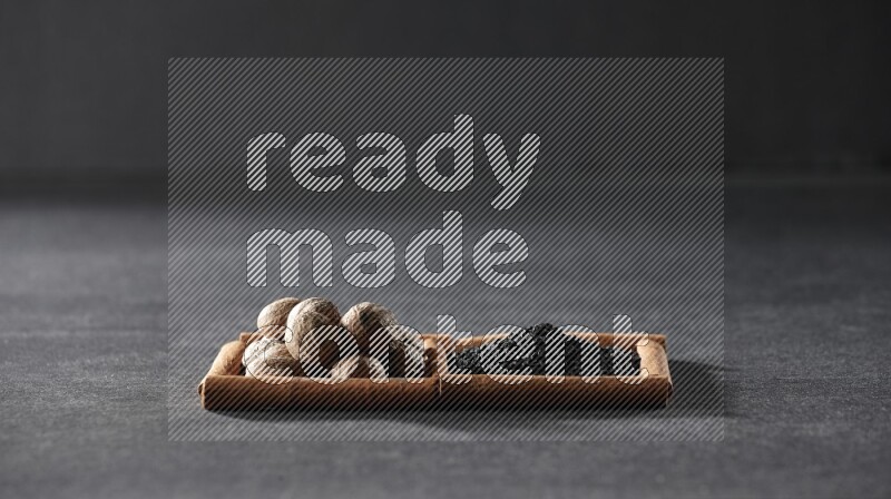 2 squares of cinnamon sticks full of black seeds and nutmeg on black flooring