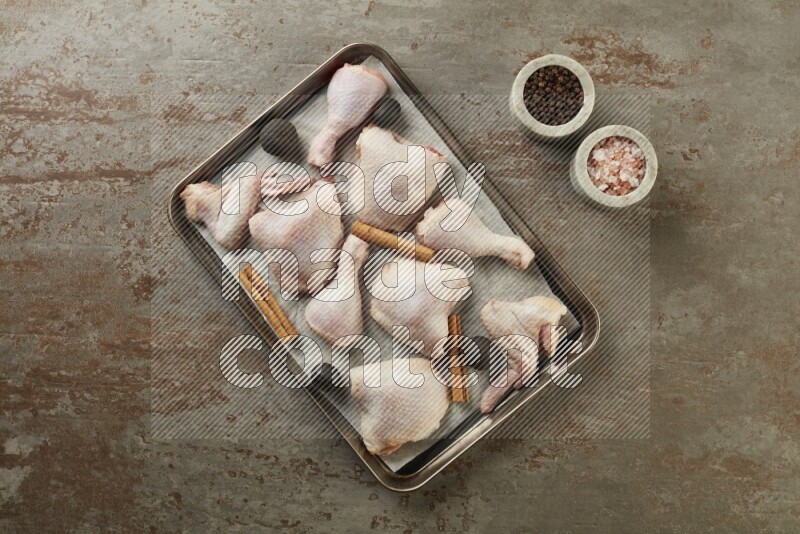 Mixed fresh chicken pieces in an oven tray on a textured rustic background