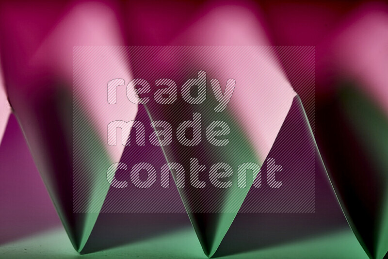 A close-up abstract image showing sharp geometric paper folds in green and purple gradients