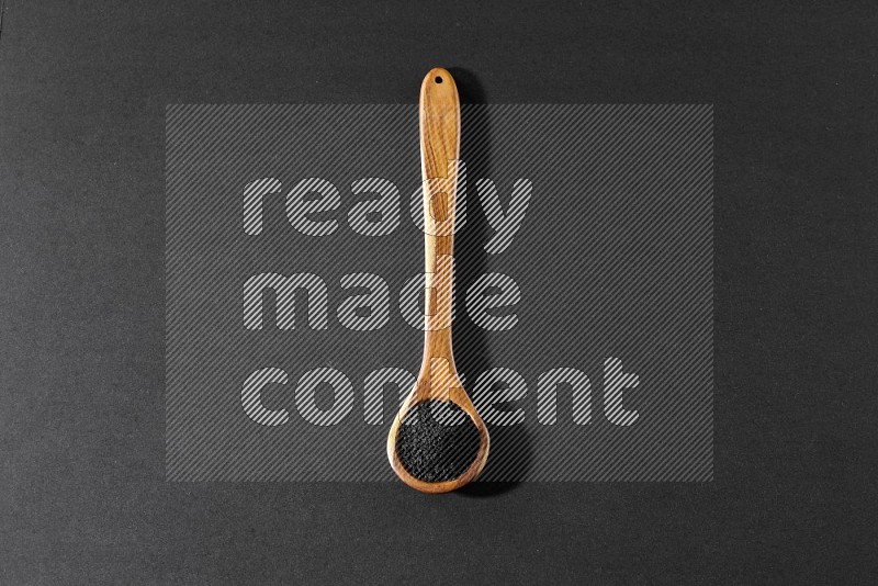 A wooden ladle full of black seeds on a black flooring