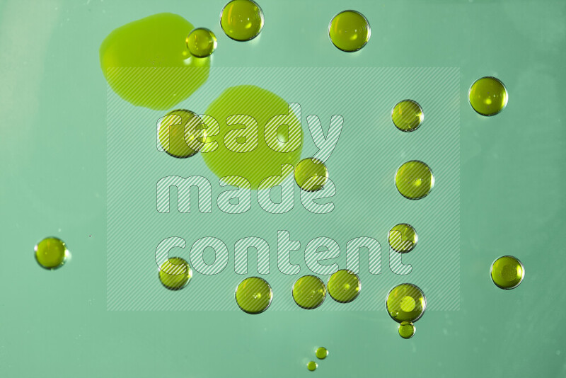 Close-ups of abstract yellow watercolor drops on oil Surface on green background
