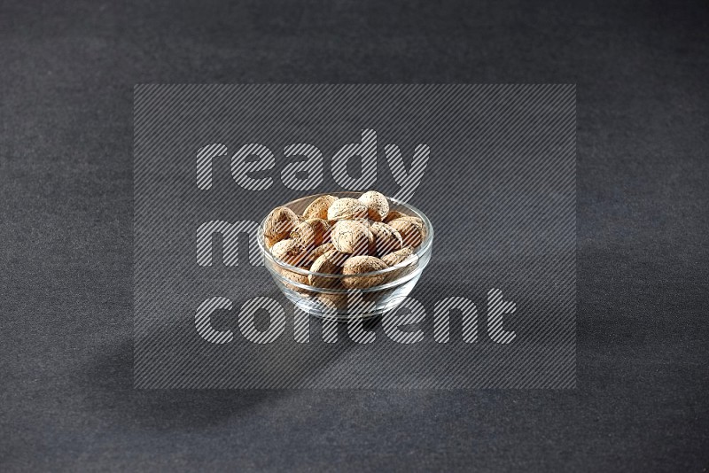 A glass bowl full of almonds on a black background in different angles