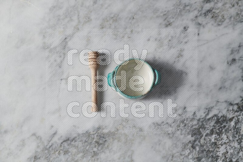 Multicolored pottery bowl with wooden honey dipper on the side on grey marble background