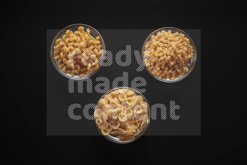 Different pasta types in glass bowls on black background