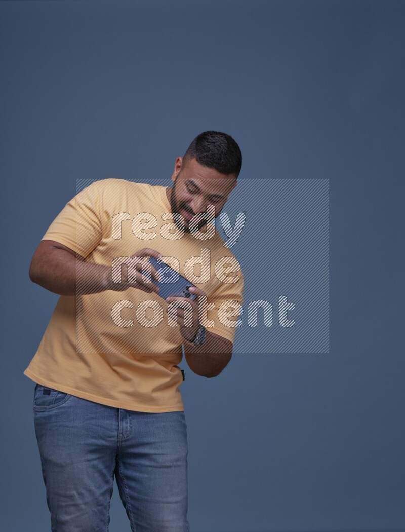 A man Playing Games on Smartphone on Blue Background wearing Orange T-shirt