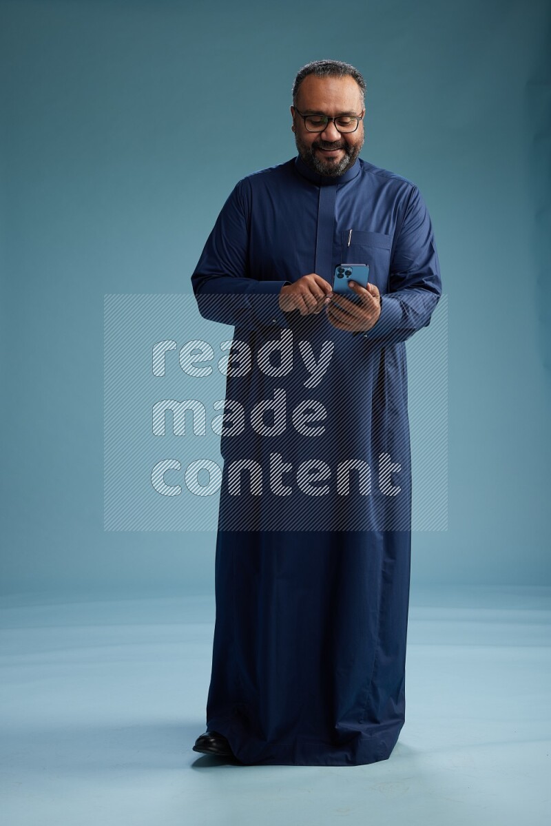 Saudi Man without shimag Standing texting on phone on blue background