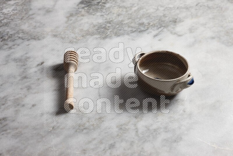 Multicolored pottery bowl with wooden honey dipper on the side on grey marble background