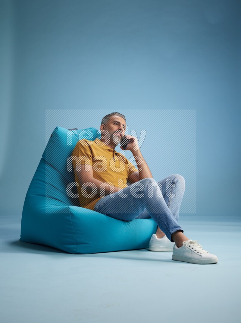 A man sitting on a blue beanbag and talking on the phone