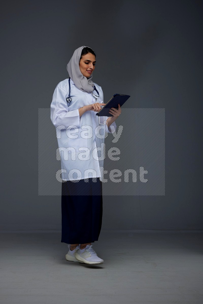 A Saudi doctor wearing a light gray head scarf standing and crossing her hands eye level on a grey background
