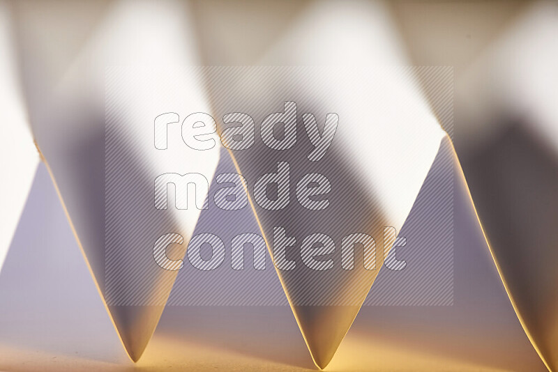 A close-up abstract image showing sharp geometric paper folds in white gradients and warm tones