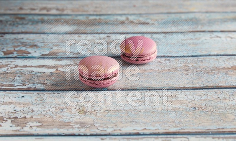 45º Shot of two Purple Strawberry macarons on light blue wooden background