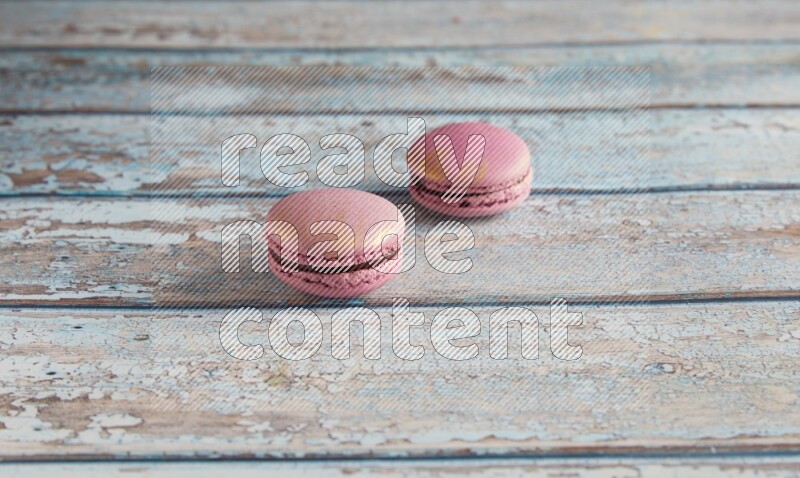 45º Shot of two Purple Strawberry macarons on light blue wooden background