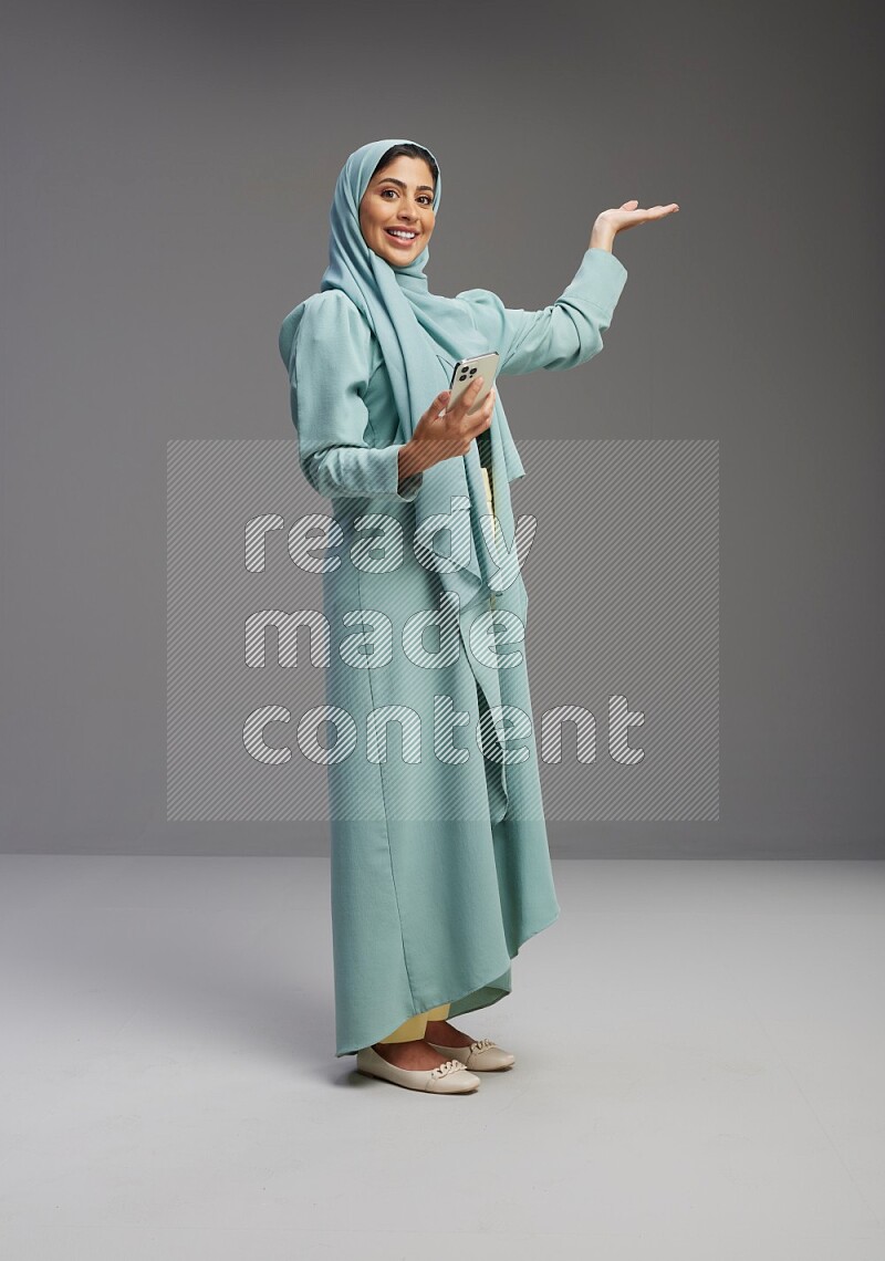 Saudi Woman wearing Abaya standing texting on phone on Gray background