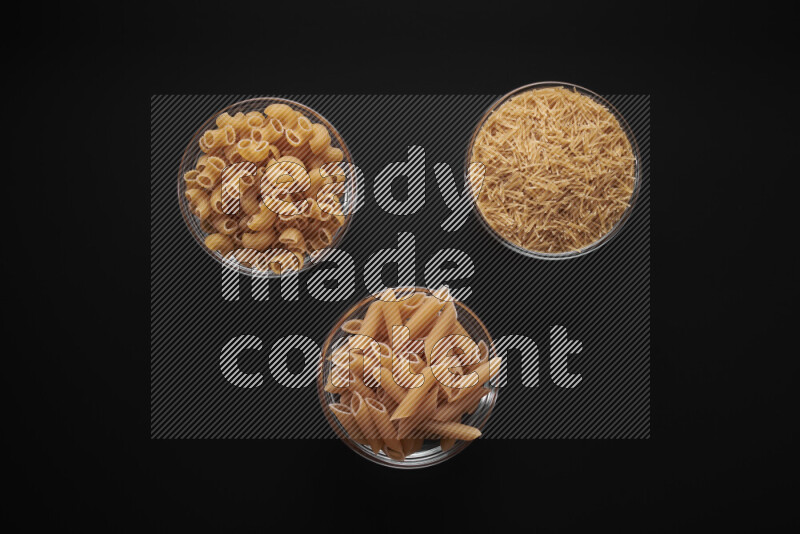 Different pasta types in glass bowls on black background