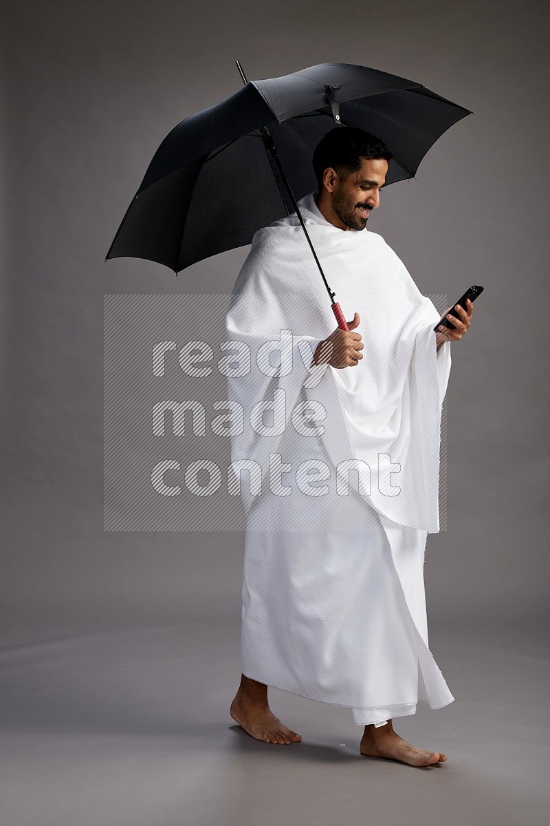 A man wearing Ehram Standing holding umbrella on gray background