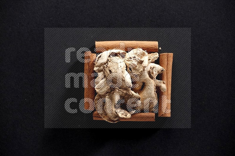 A single square of cinnamon sticks full of dried ginger on black flooring