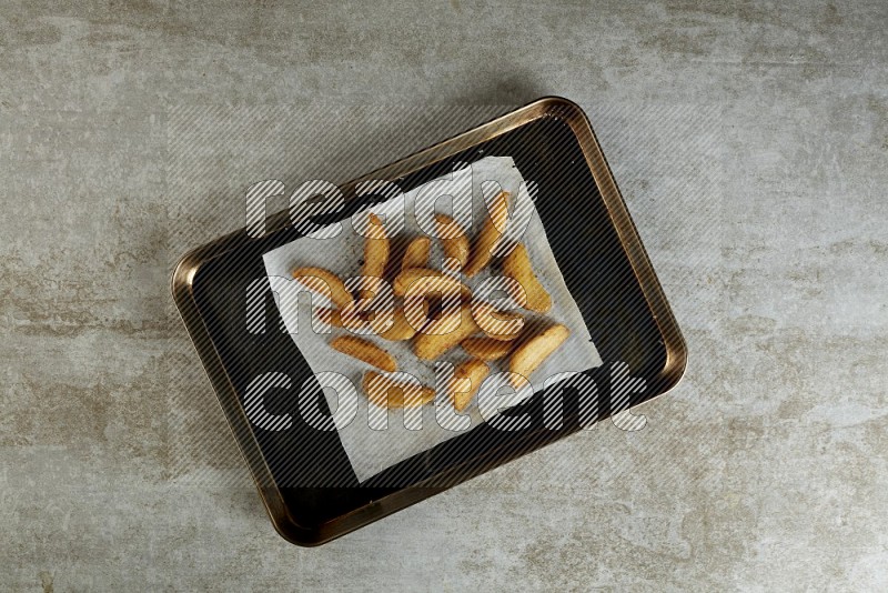 wedges potato on parchment paper in a black stainless steel rectangle tray on grey textured counter top