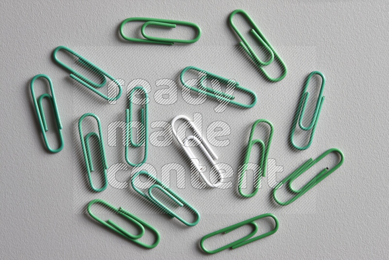 A white paperclip surrounded by bunch of green paperclips on grey background
