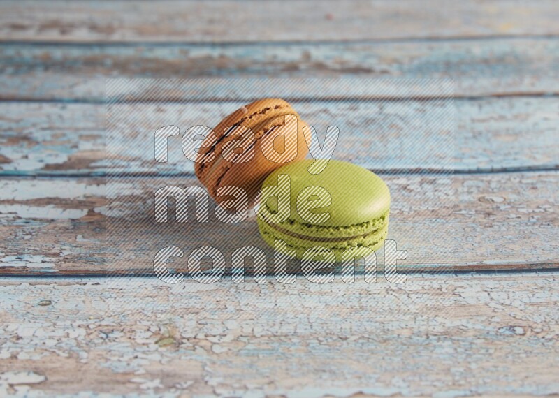 45º Shot of of two assorted Brown Irish Cream, and Green Pistachio macarons  on light blue background