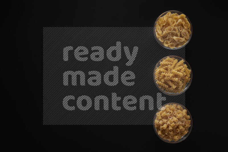 Different pasta types in 3 glass bowls on black background
