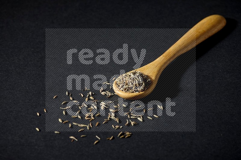 A wooden spoon full of cumin seeds on black flooring