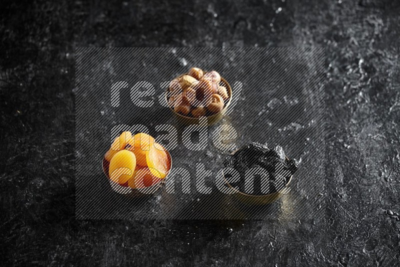 Dried fruits in metal bowls in a dark setup