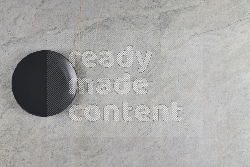A black ceramic circular plate on grey marble background