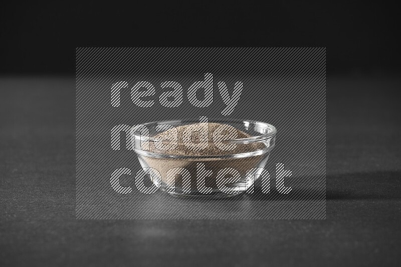 فلفل أسود مطحون في وعاء زجاجي علي خلفية سوداء