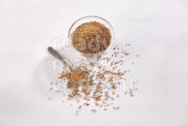 A glass bowl and metal spoon full of mustard seeds on a white flooring in different angles