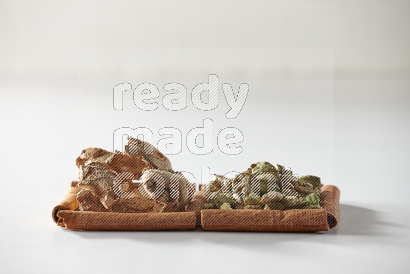 مربعان من أعواد القرفة ممتلئان بحبوب الهيل والزنجبيل المجفف علي خلفية بيضاء