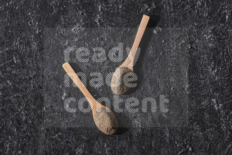 بودرة الفلفل الأسود في ملعقتان خشبيتان علي خلفية سوداء