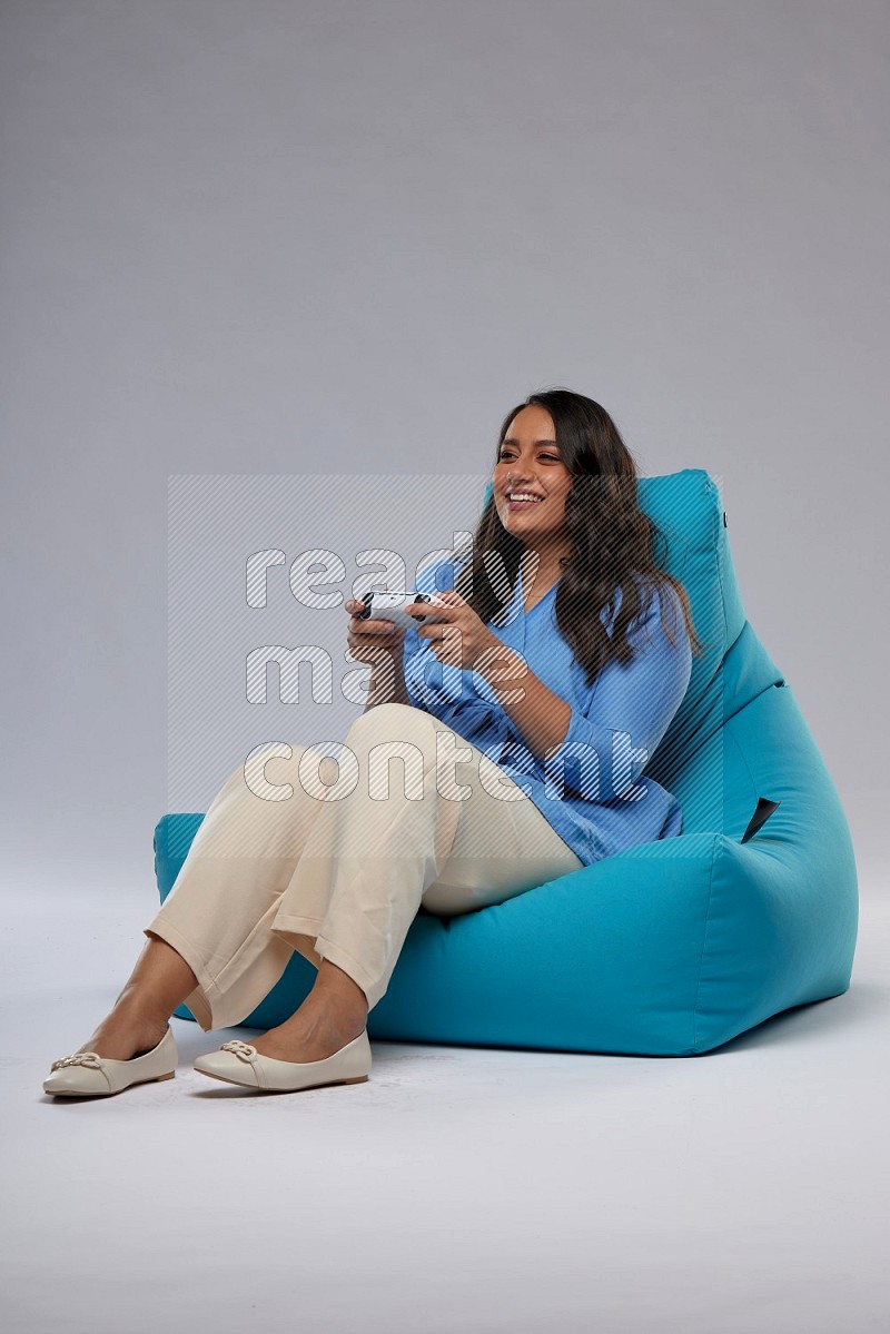 A woman sitting on a blue beanbag and gaming with joystick