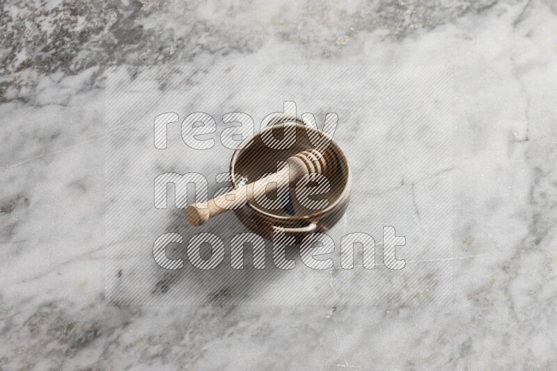 Multicolored pottery bowl with wooden honey dipper in it on grey marble background