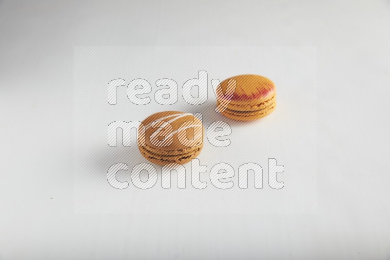45º Shot of of two assorted Brown Irish Cream, and Orange Exotic macarons on white background